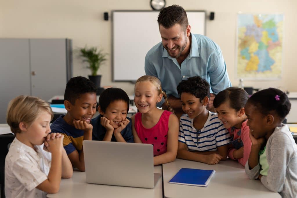 Male teacher teaching kids on laptop in classroom » Sistema Saberes | Plataforma Educativa para Colegios Factores que se deben tener en cuenta para calificar la calidad educativa.